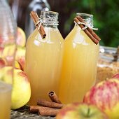 Cloudy apple juice in glass bottles, fresh apples, cinnamon sticks