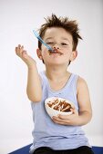 Kleiner Junge hält Löffel mit Schokopudding im Mund