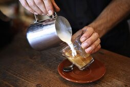Barista pouring frothed milk into coffee