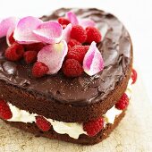 Heart-shaped chocolate cake with raspberries, cream and rose petals