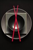 Black plates and bowl and red chopsticks (overhead view)