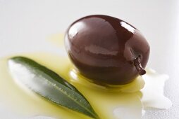 Black olive with olive oil and olive leaf (close-up)