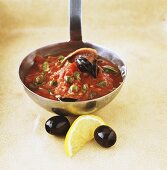 Tomato sauce with anchovies, capers and olives on ladle