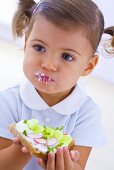 Little girl eating slice of bread with quark, cucumber and radishes