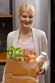 Blond woman holding bag of shopping in kitchen