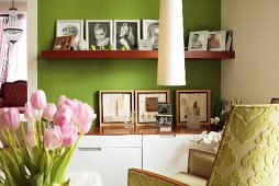 Modern cabinet with matching wooden shelf holding family photos against green-painted wall