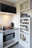 Detail of a designer kitchen with wall-mounted cupboard above ceramic hob and recessed shelving for spices