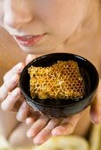 A woman holding a honey bowl with a honeycomb inside