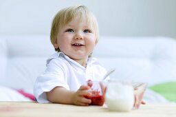 A small child holding a glass of squashed strawberries