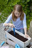 A girl making holes in soil for seeds