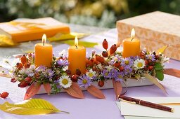 Autumnal arrangement of flowers, rose hips and candles on table