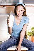 Lachende Frau sitzt in der Küche mit einer Milchflasche
