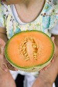 Child holding half a cantaloupe melon