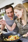 Young couple tasting vegetables from wok