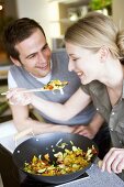 Young couple tasting vegetables cooked in wok