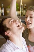 Young woman feeding man a strand of spaghetti