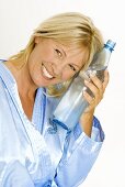 Lächelnde Frau kühlt sich mit einer Flasche Mineralwasser ab