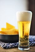 A glass of lager in front of a plate of tortilla chips