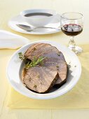 Several slices of roast beef with gravy and herbs