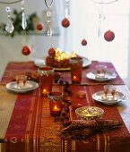 Laid table with Christmas decorations and tealights in glasses (in red)