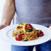 Mann hält Teller mit Spaghetti, Kirschtomaten und Basilikum