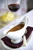 Gravy in a gravy boat with a glass of red wine in the background