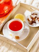 A cup of rosehip tea with candied sugar and lemon on a tray