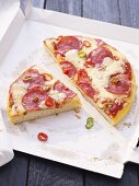 Pizza mit Salami und Chiliringen auf Pizzakarton