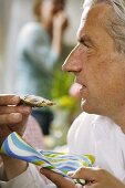 Grauhaariger Mann isst eine Auster