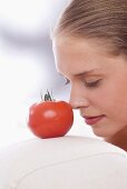 Junge Frau berührt mit ihrer Nasenspitze eine Tomate