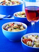 Pasta salad in blue bowls and glass of rosé wine on table