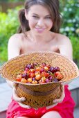 Young woman holding straw hat full of sweet cherries