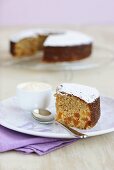 Piece of apricot orange cake with icing sugar in front of rest of cake