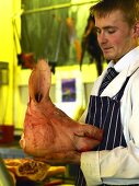 A butcher holding a hog's head in his hands at a Farmer's Market in England