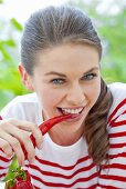 A girl bitting into a chilli pepper