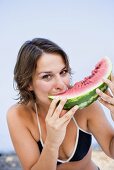 Junge Frau isst ein Stück Wassermelone am Strand