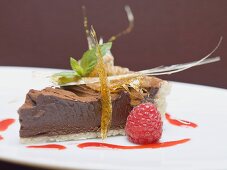 A piece of chocolate torte with a caramel fan and a raspberry