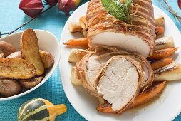 Bacon-wrapped turkey breast (partly carved) on root vegetables