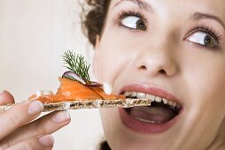 Young woman eating crispbread with salmon