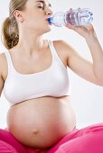 Schwangere Frau trinkt Mineralwasser aus der Flasche