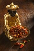 Statuette with bowl of chilli flakes, chillies on wooden background