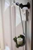 Candle and white spruce twigs in enamel ladle on door handle