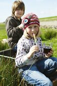 Geschwister mit Süssigkeiten und Kinderpunsch auf der Wiese