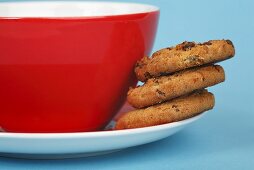 Three chocolate chip cookies on a saucer with cup