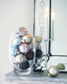 Christmas baubles in glass vase beside candle on mantelshelf
