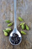 Cardamom seeds in spoon among cardamom pods