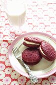 Raspberry whoopie pies on a plate with a fork and a glass of milk