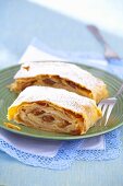 Two slices of apple strudel with hazelnuts, raisins and icing sugar