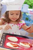 A little girl spreading tomato sauce onto pizza dough