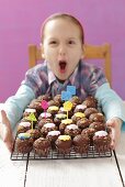 A girl with a wire rack of mini chocolate cupcakes